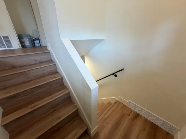 Hardwood-finish stairs with a white stairwell wall and a black handrail