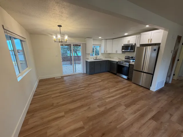 Open-concept kitchen and dining area featuring wood-finish flooring, two-tone cabinetry, stainless steel appliances, and a sliding glass door leading to a patio