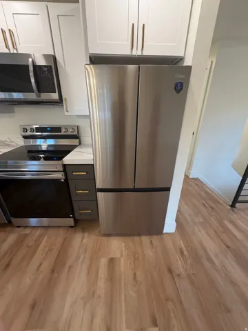 Stainless steel French door refrigerator, wood-finish flooring, white upper cabinetry, grey lower cabinetry, and a built-in microwave