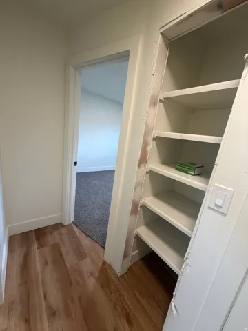 Wood-finish flooring with white baseboards, a white painted doorway, and built-in shelving