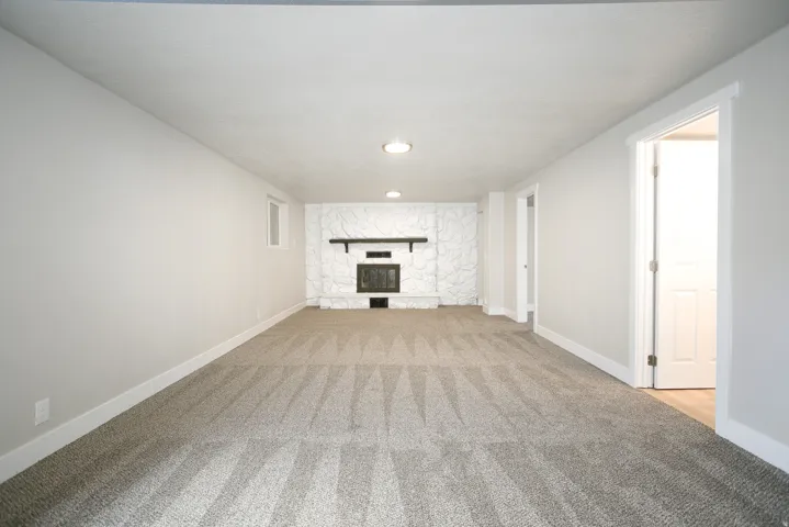 Spacious room featuring broadloom carpeting and a stone fireplace with a dark wood mantel