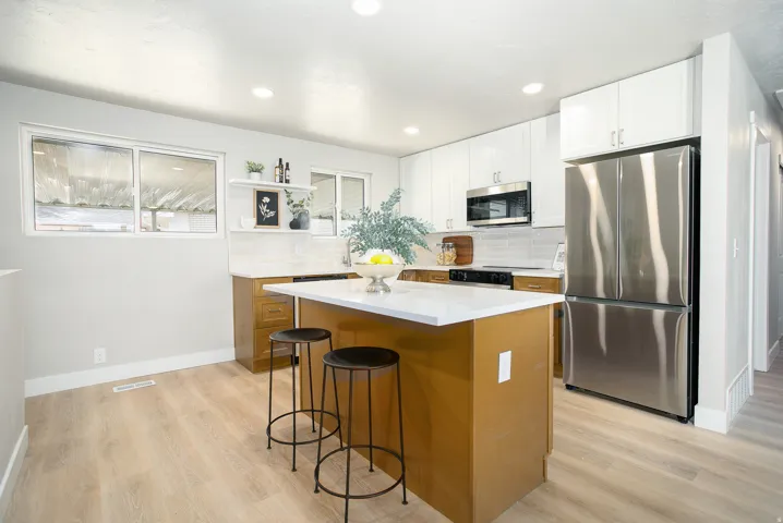 Kitchen featuring wood-finish flooring, white shaker-style upper cabinetry, stainless steel appliances, and a central island with a white countertop