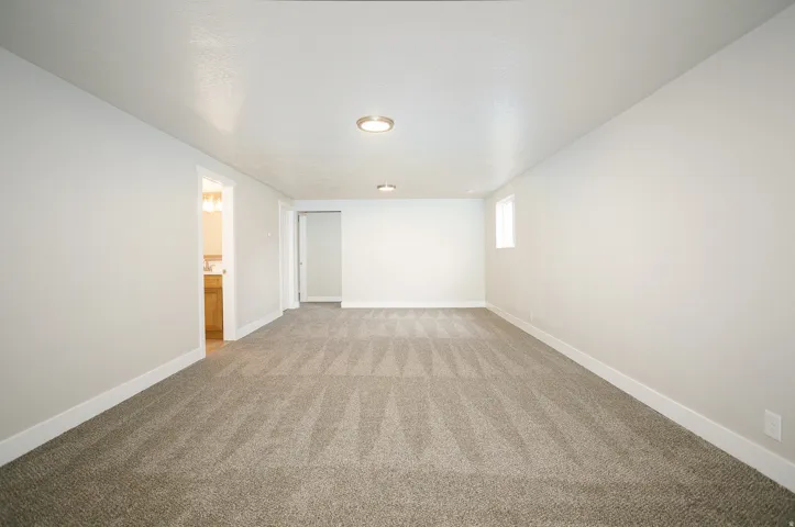Spacious room featuring neutral carpet flooring, recessed lighting, and a small window for natural illumination