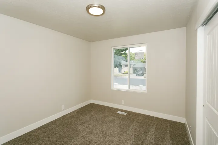 Carpeted flooring, neutral wall tones, modern flush mount ceiling light, sliding window with white frame, and a white barn door