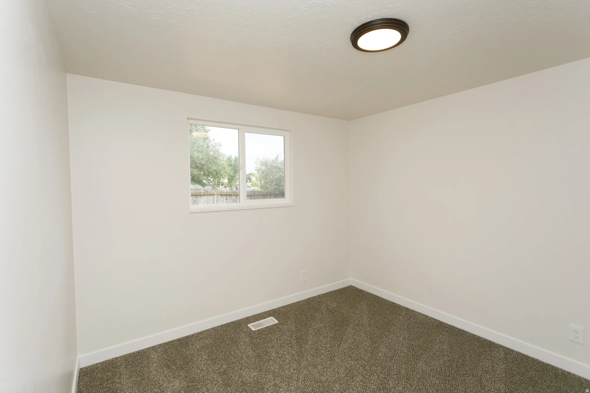 Neutral paint, textured ceiling, brown flush-mount ceiling light, white window trim, and gray carpet