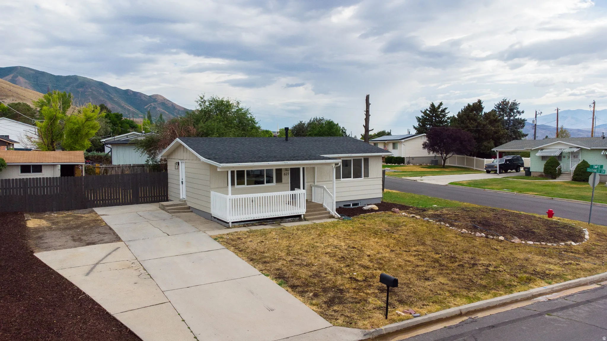 Single-story residence featuring a covered front porch with white railing, a dark shingle roof, and a concrete driveway