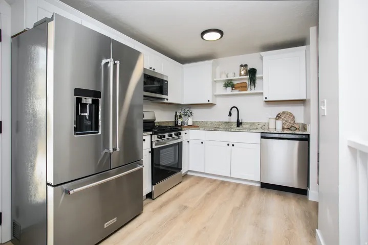 Stainless steel appliances, white cabinetry, light wood-finish flooring, and open shelving
