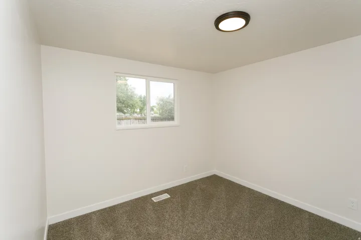 Neutral paint, textured ceiling, brown flush-mount ceiling light, white window trim, and gray carpet
