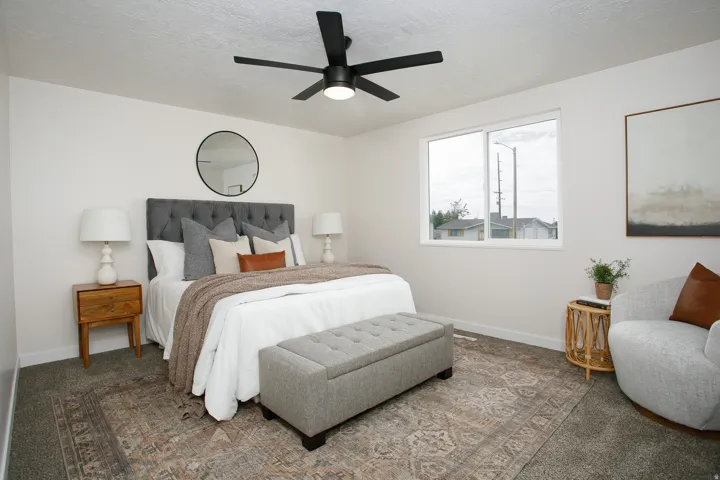 Window with white framing, gray upholstered headboard, black ceiling fan with integrated lighting