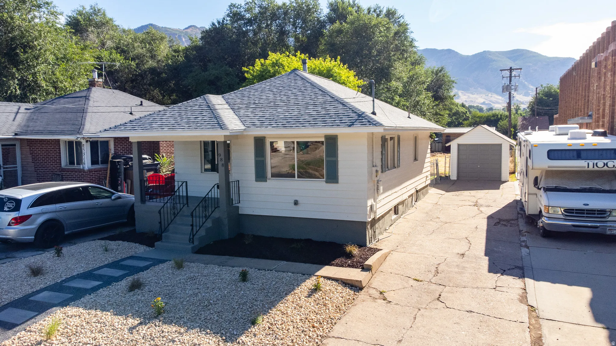 White exterior siding with green shutters, covered front entry, new roof, detached garage, and a gravel front yard with a paver walkway