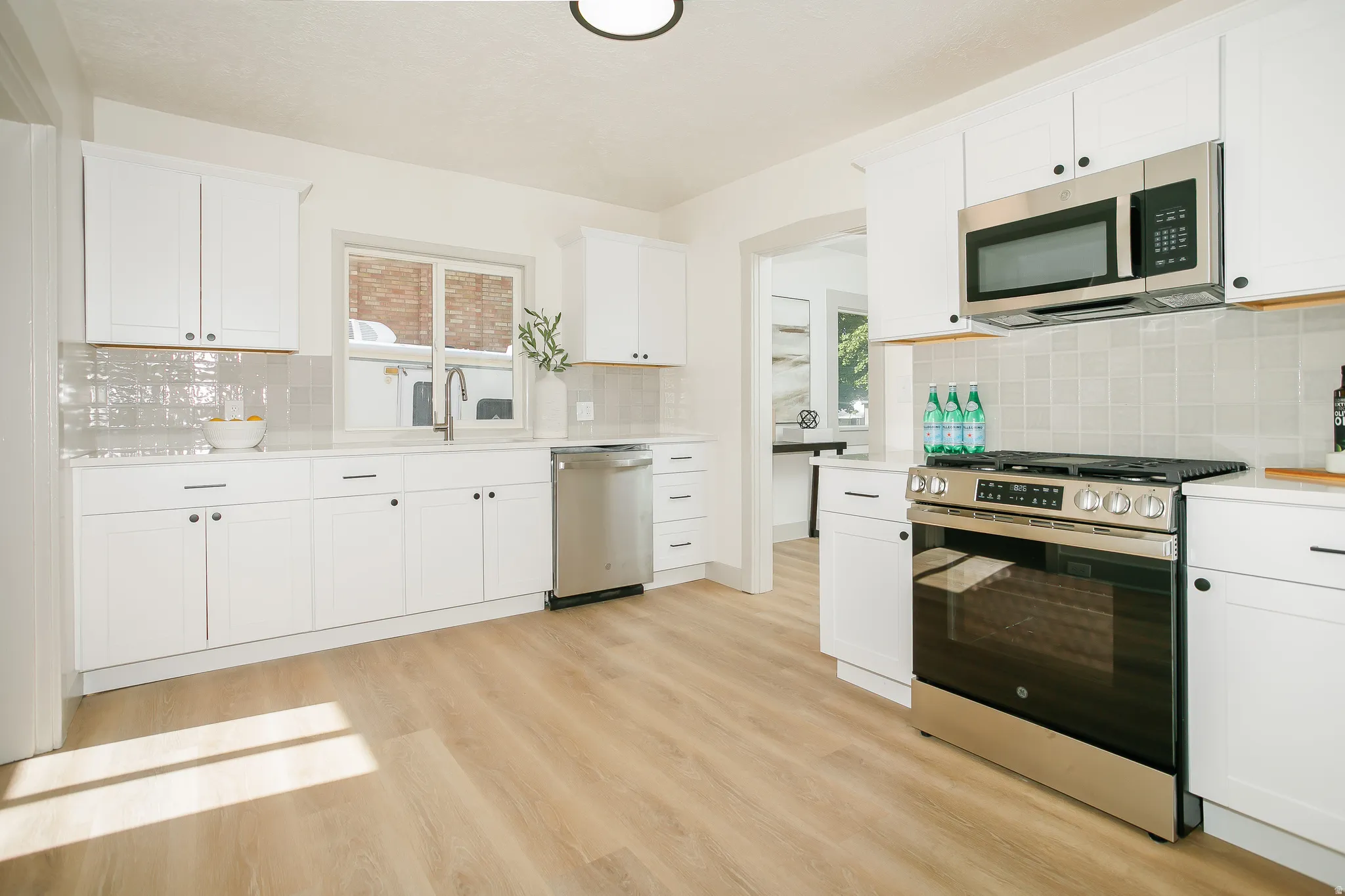 Kitchen featuring white shaker cabinetry, stainless steel appliances, light wood-finish flooring, and a subway tile backsplash