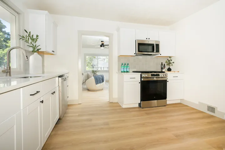 White cabinetry with black hardware, stainless steel appliances, light wood-finish flooring, light countertop, and a tiled backsplash