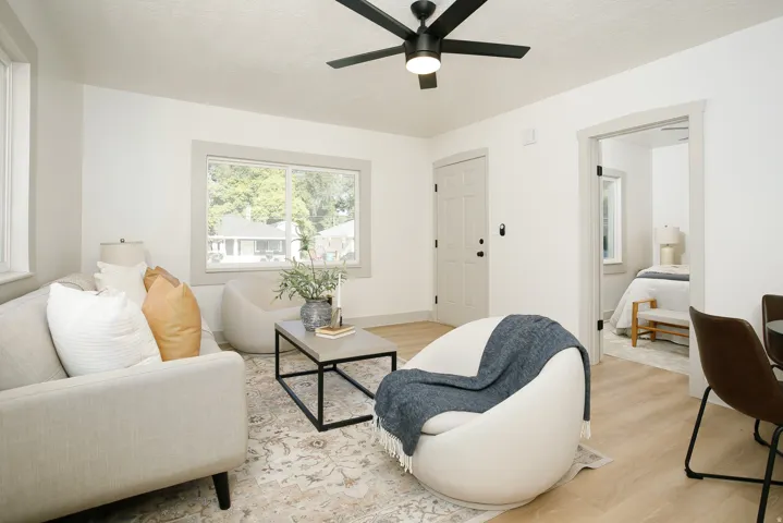 Bright living area featuring wood-finish flooring, a ceiling fan, and a paneled entry door with dark hardware