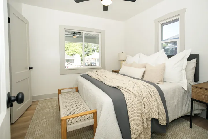 White walls, light wood-finish flooring, two windows with gray trim, a ceiling fan, and a white interior door with black hardware