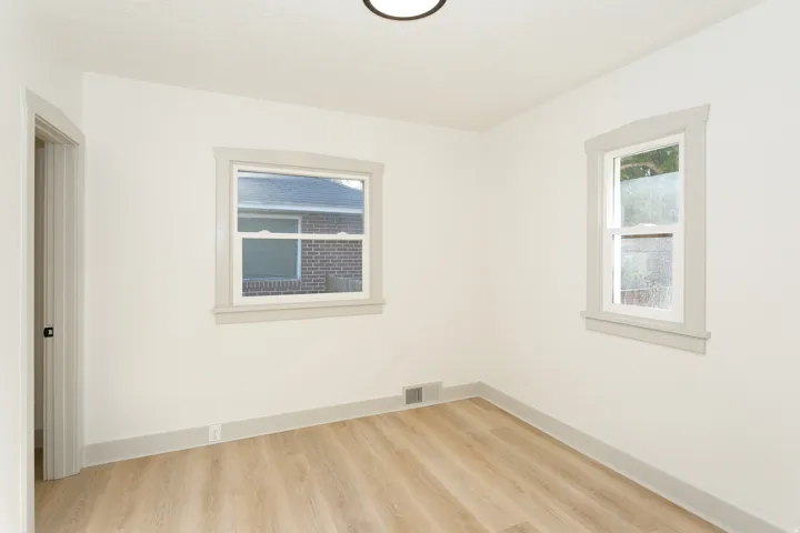 Neutral wall paint, wood-finish flooring, two large windows, white trim, and a contemporary ceiling light fixture