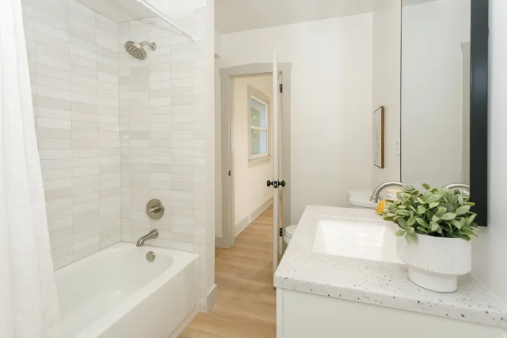 White bathtub with brushed nickel fixtures, subway tile surround, white vanity, integrated sink, and light-toned wood-finish flooring