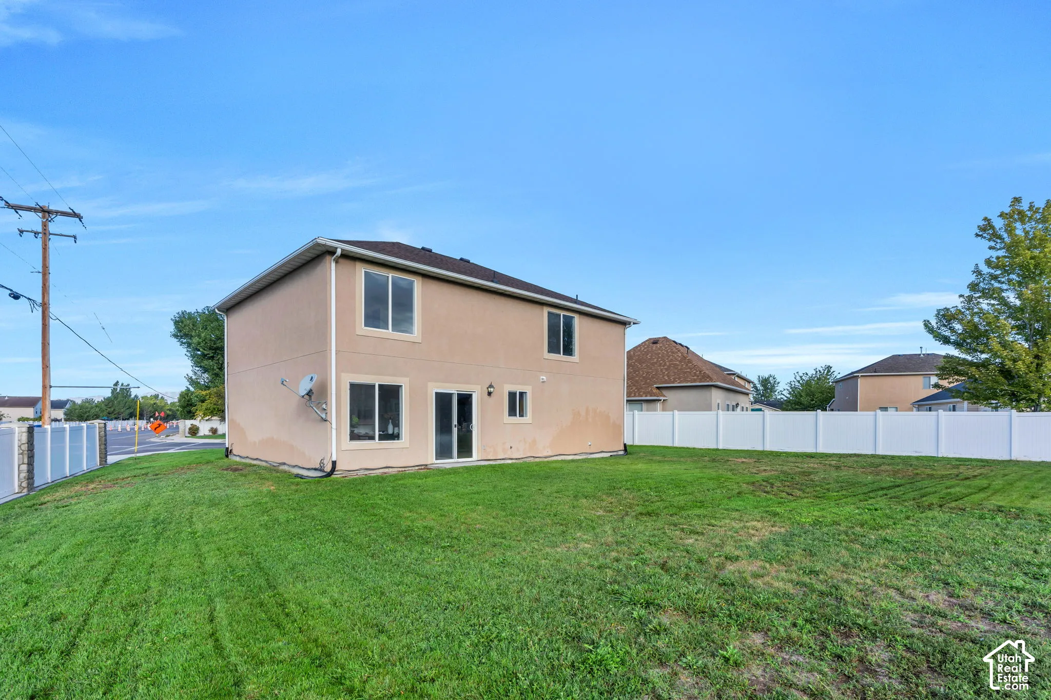 Expansive backyard with a manicured lawn, full fencing, and a two-story residence featuring multiple windows and a sliding glass door