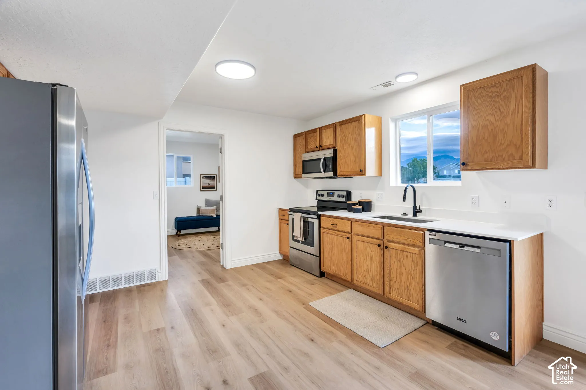 Kitchen featuring wood-finish cabinetry, stainless steel appliances, white countertops, and wood-finish flooring