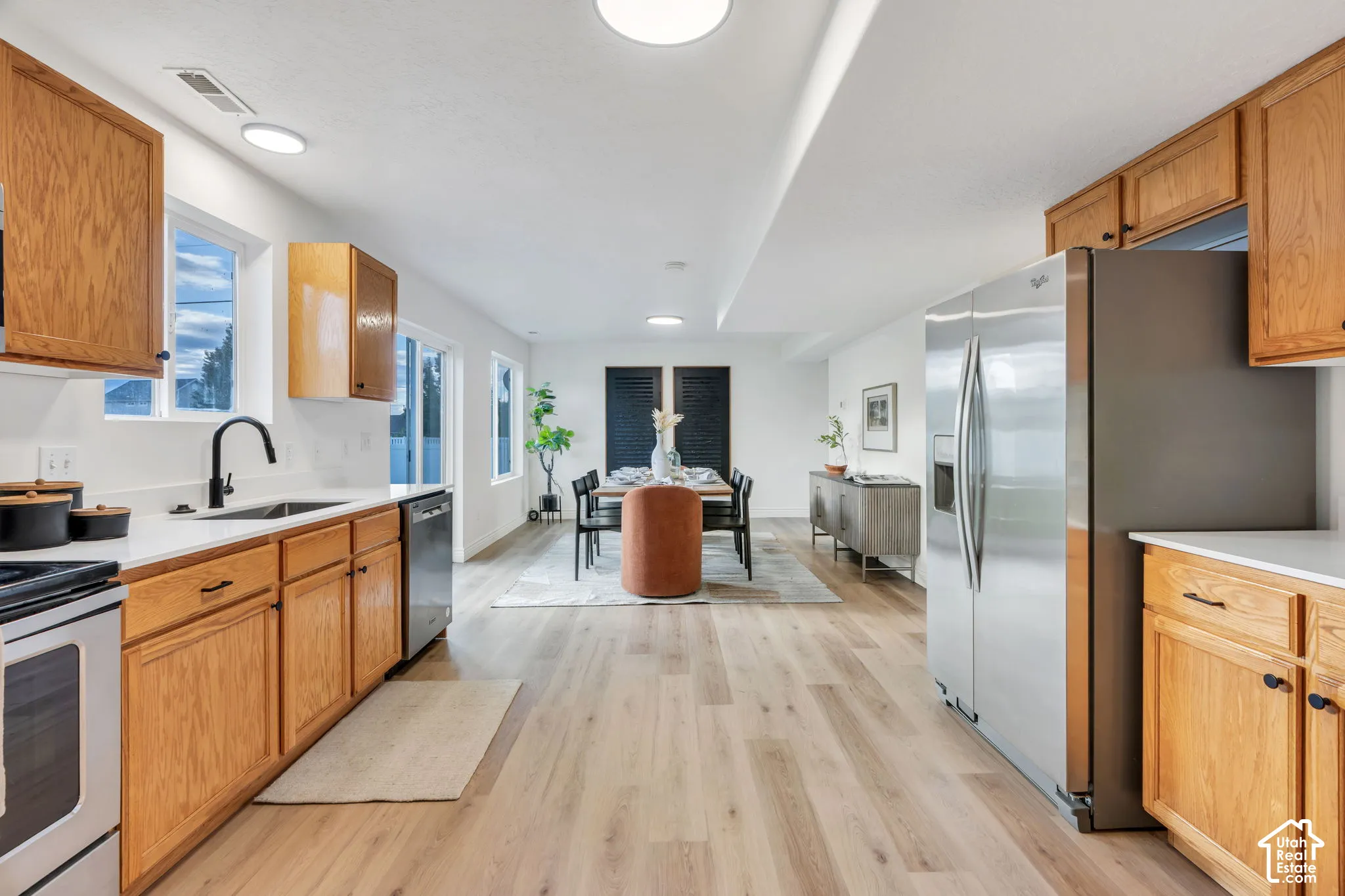 Kitchen featuring wood-finish cabinetry, stainless steel appliances, a black gooseneck faucet, and light countertops