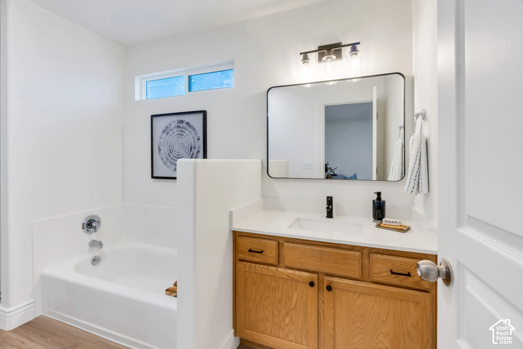 White vanity with wood-finish cabinetry, a rectangular undermount sink, and a black-framed mirror