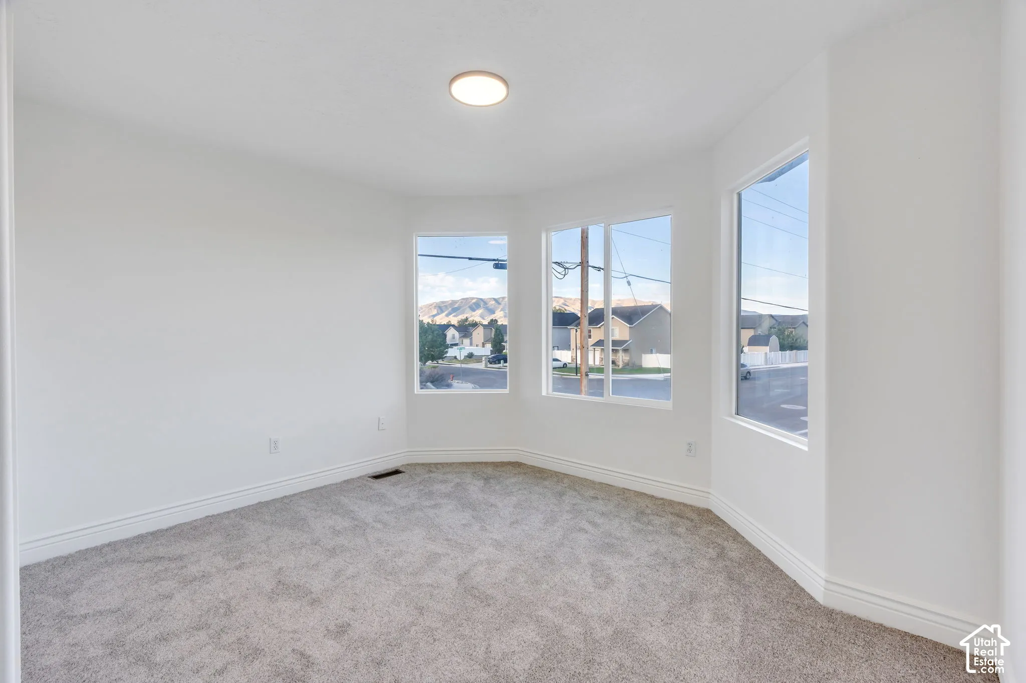 Recessed lighting fixture, three large windows, textured carpeting, and white trim