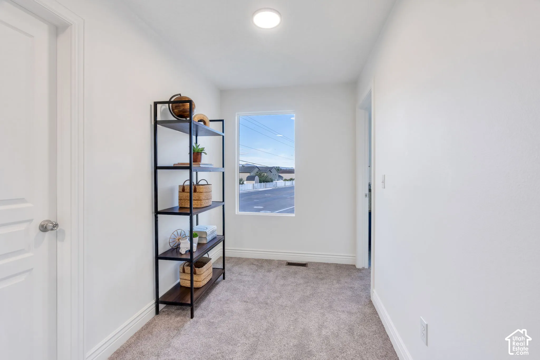 Carpeted hallway with a single rectangular window, recessed lighting, and a paneled interior door