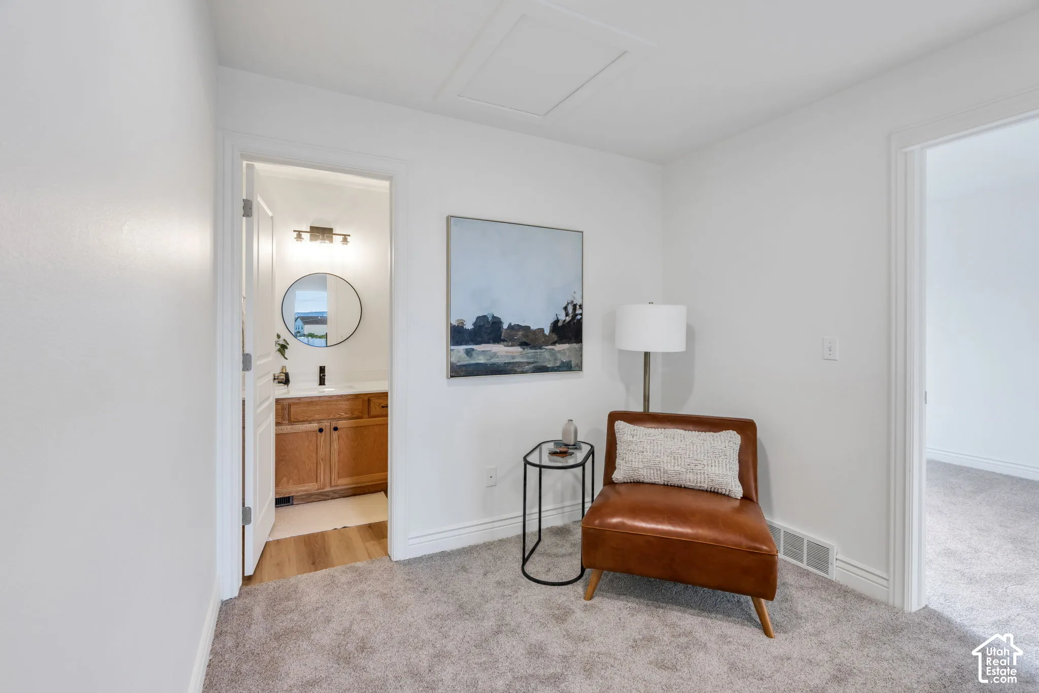 Carpeted interior area with an entry to a bathroom featuring a wood-finish vanity and round mirror