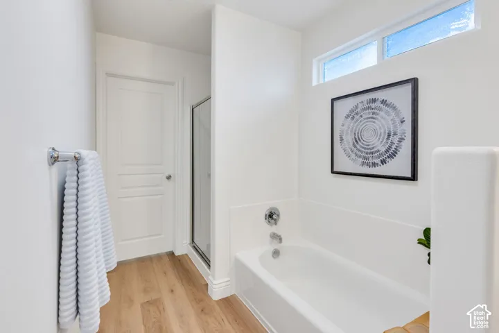 White bathtub with chrome fixtures, wood-finish flooring, and a transom window