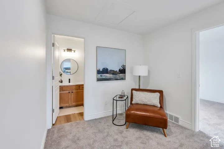 Carpeted interior area with an entry to a bathroom featuring a wood-finish vanity and round mirror