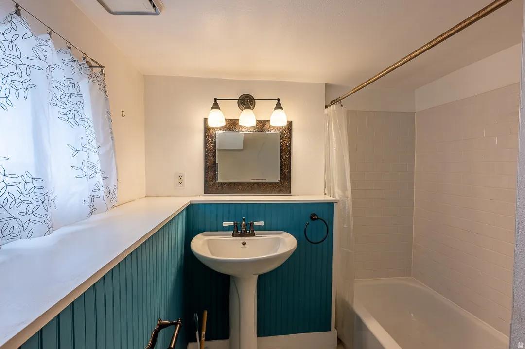 White pedestal sink with a dual-handle faucet, accented by a bronze-framed mirror and a three-light vanity fixture