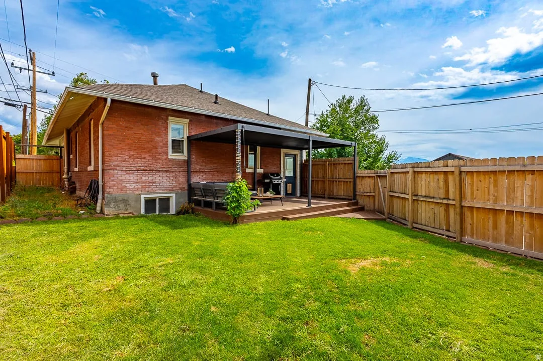 Red brick exterior with a rear deck featuring a dark pergola, a full wood fence, and a green lawn