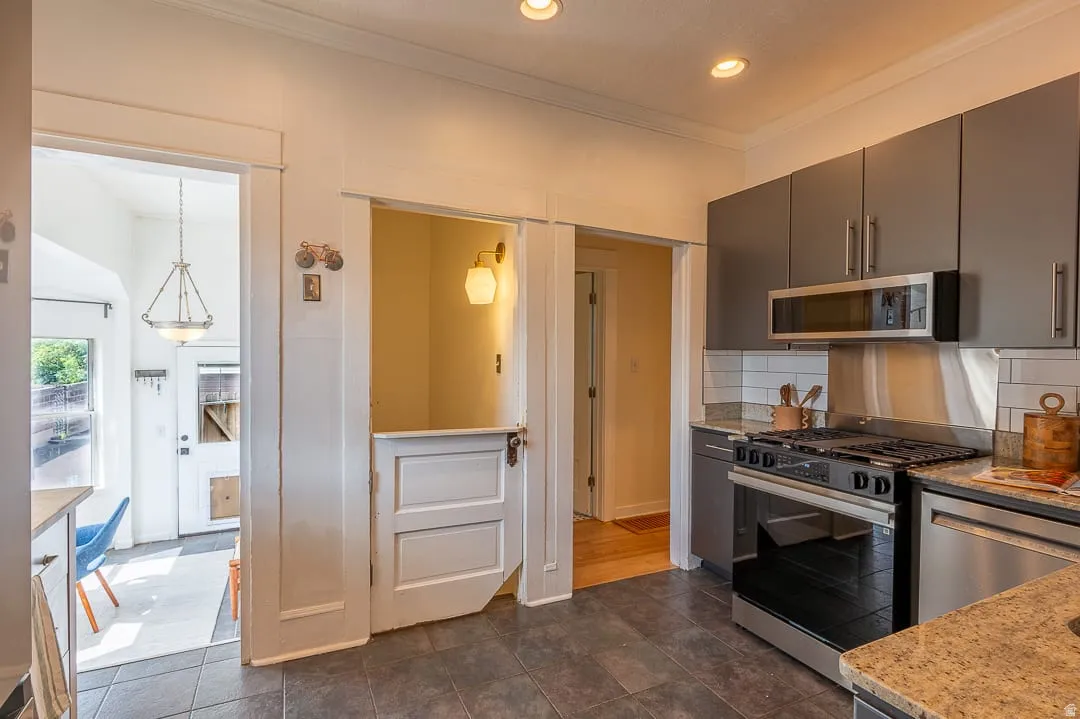 Kitchen featuring dark gray cabinetry, stainless steel appliances, granite countertops, and subway tile backsplash