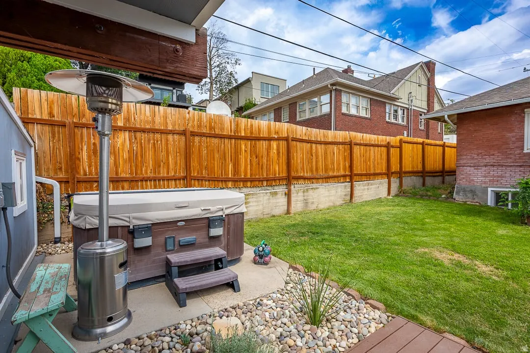 Expansive backyard oasis featuring a wood-finish privacy fence, mature landscaping with lush lawn, river rock hardscaping, and a hot tub with seating area