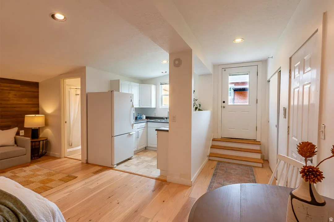 Open-concept studio with wood-finish flooring throughout, featuring a galley kitchen with white cabinetry and refrigerator, and recessed ceiling lighting