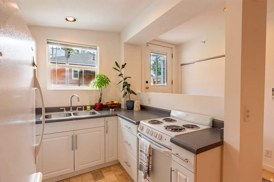 White cabinetry, dual basin stainless steel sink, dark countertops, built-in range, and a window with natural light