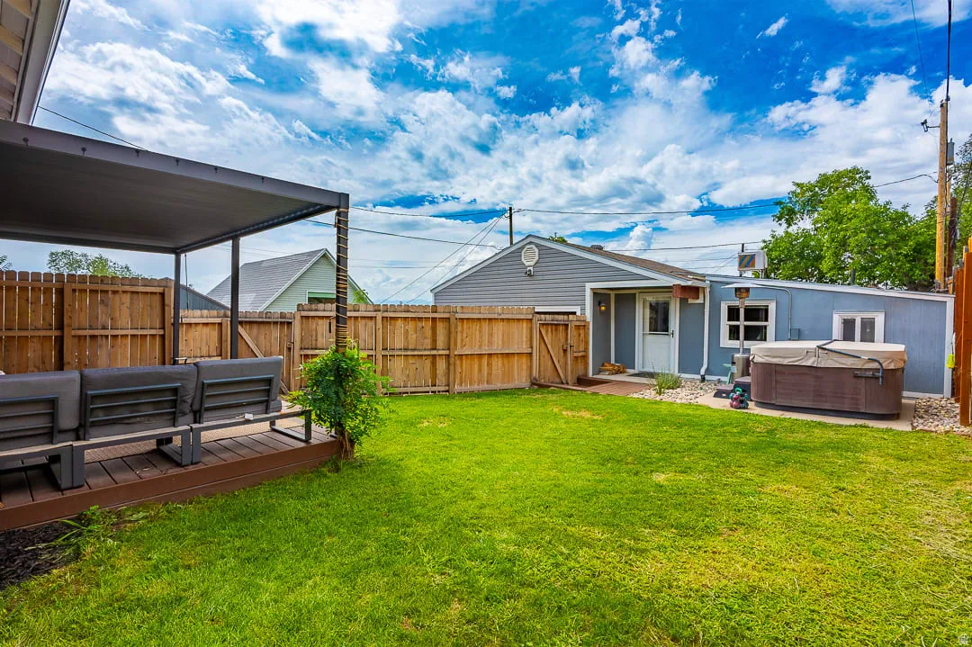 Expansive backyard featuring a lush lawn, privacy fencing, a covered patio with composite decking, and an outdoor spa