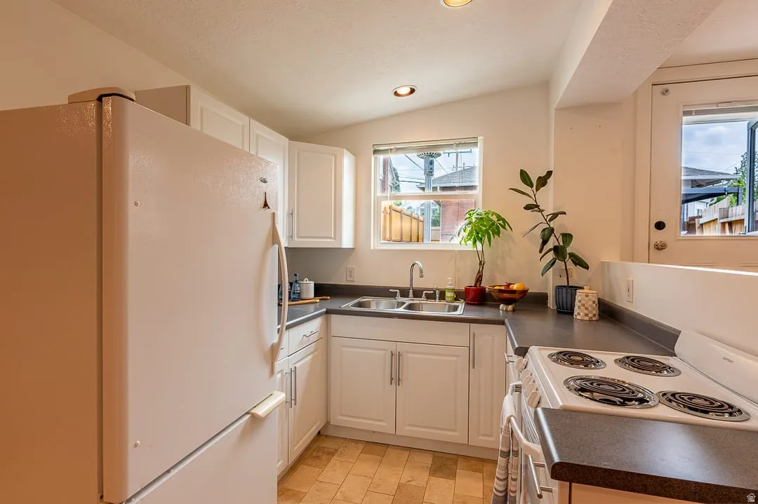 Compact kitchen featuring white cabinetry with brushed nickel hardware, black countertops, electric range with coil burners, and refrigerator