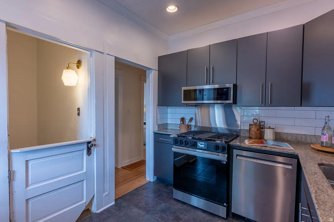 Kitchen featuring dark gray cabinetry, stainless steel appliances, light granite-style countertops, white subway tile backsplash, and dark tile flooring