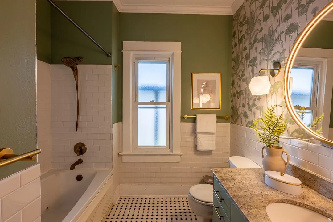 White subway tile wainscoting, black and white mosaic tile flooring, built-in bathtub with bronze-finish fixtures, single vanity with light-colored countertop, and a window with white trim
