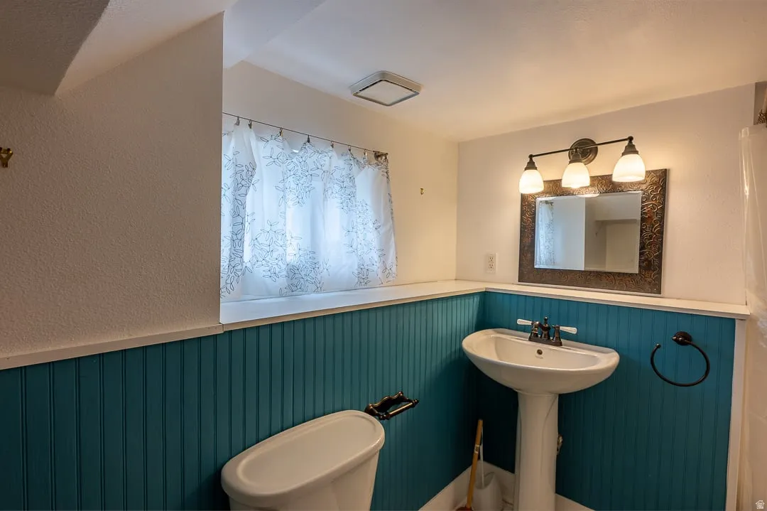 Pedestal sink, wall-mounted light fixture, decorative mirror, and beadboard wainscoting