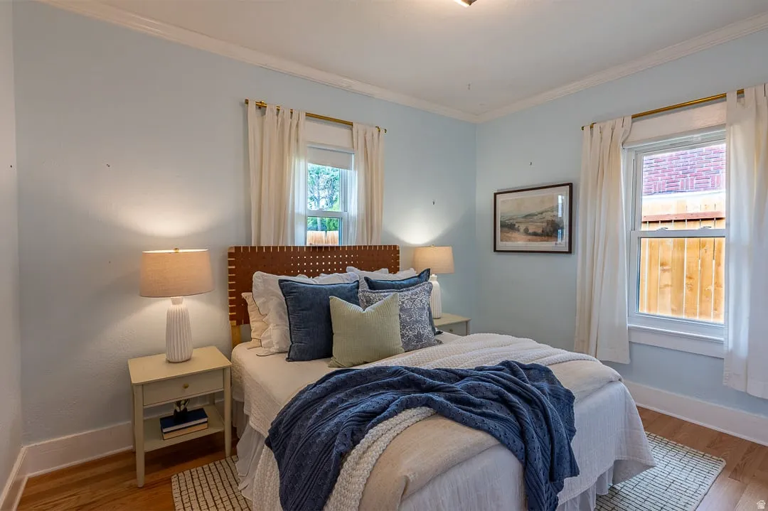 Hardwood flooring, light blue wall paint, white crown molding, and two windows with white trim