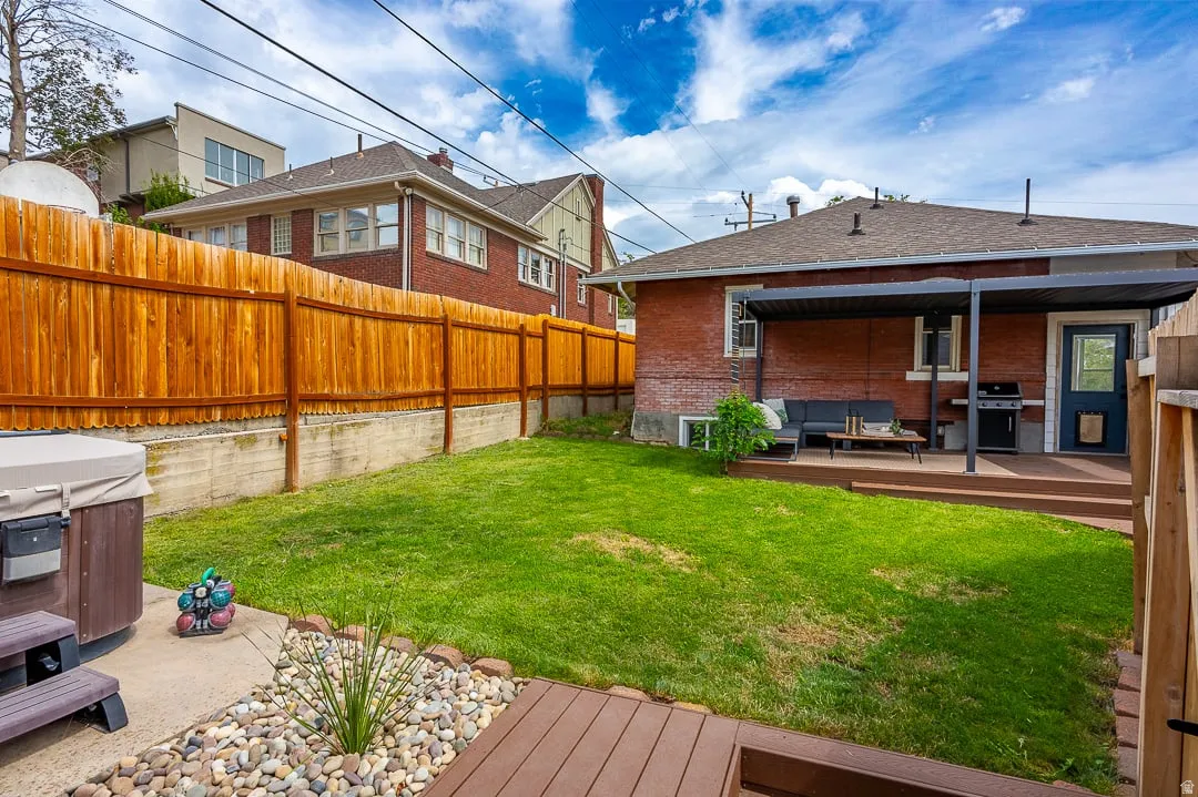 Expansive backyard featuring a manicured lawn, a brown wood fence, and a composite deck with a covered patio