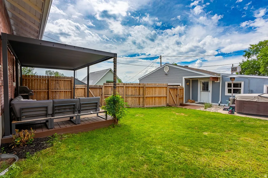 Expansive backyard featuring a covered patio, manicured lawn, full privacy fencing, and an outdoor spa
