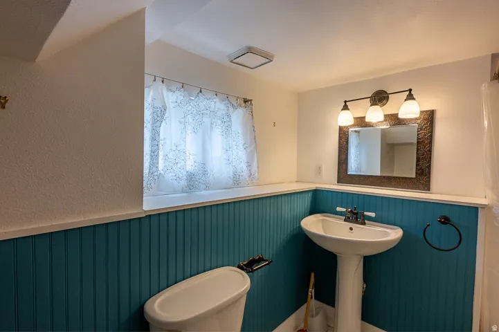 Pedestal sink, wall-mounted light fixture, decorative mirror, and beadboard wainscoting