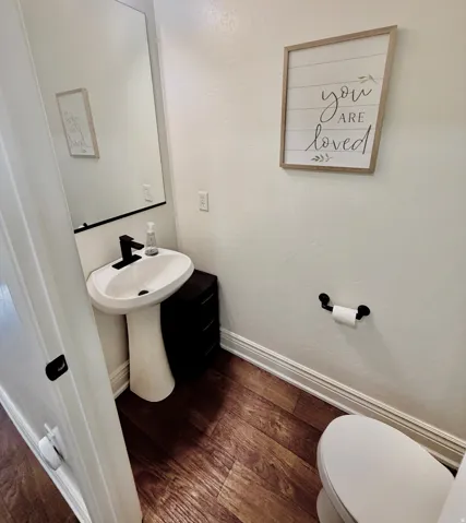 Pedestal sink with a matte black faucet, dark wood-finish flooring, white wall paint, and white trim