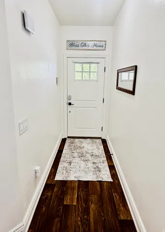 Wood-finish flooring with white baseboards leads to a white paneled door featuring a window with grid inserts and matte black hardware