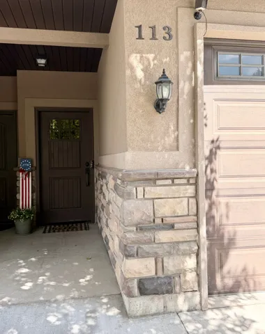 Stucco exterior with stone veneer accents, wood-paneled garage door, and covered entry with a rich wood-finish door