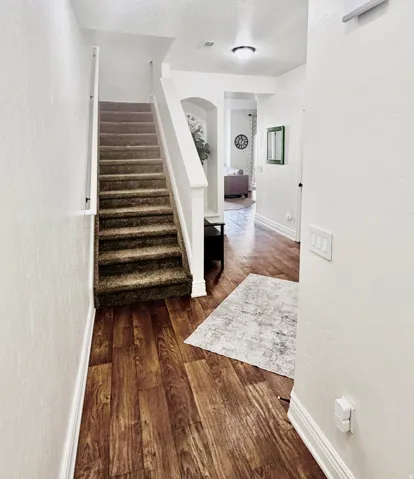 Wood-finish flooring, staircase with carpeted treads, white painted risers, and white trim