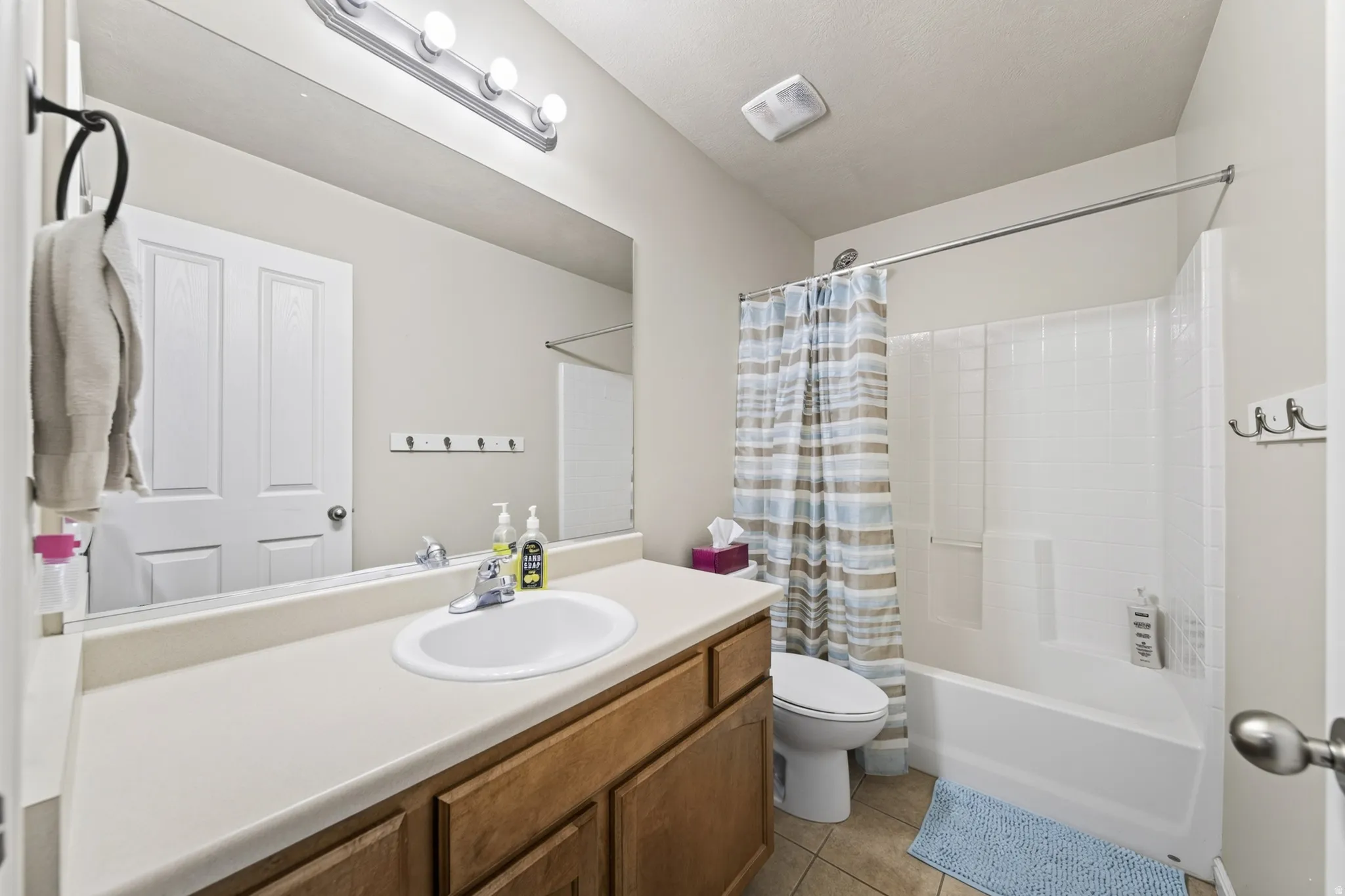 Bathroom featuring a wood-finish vanity with an integrated sink, a full-width mirror, and a shower-tub combination with a white surround