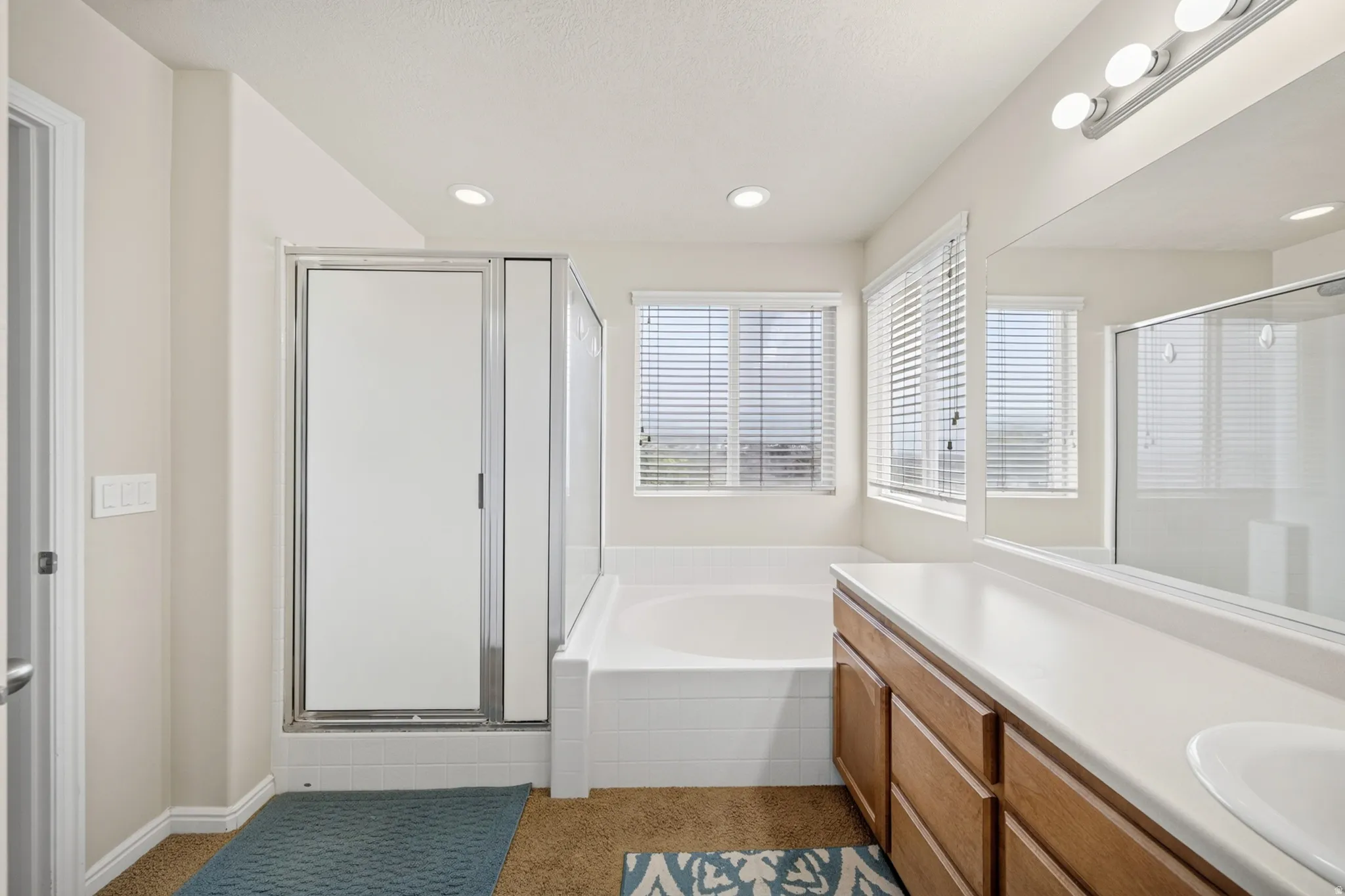 Bathroom featuring a built-in soaking tub, a separate shower enclosure with a glass door, a double vanity with wood-finish cabinetry and integrated sinks, and recessed ceiling lighting